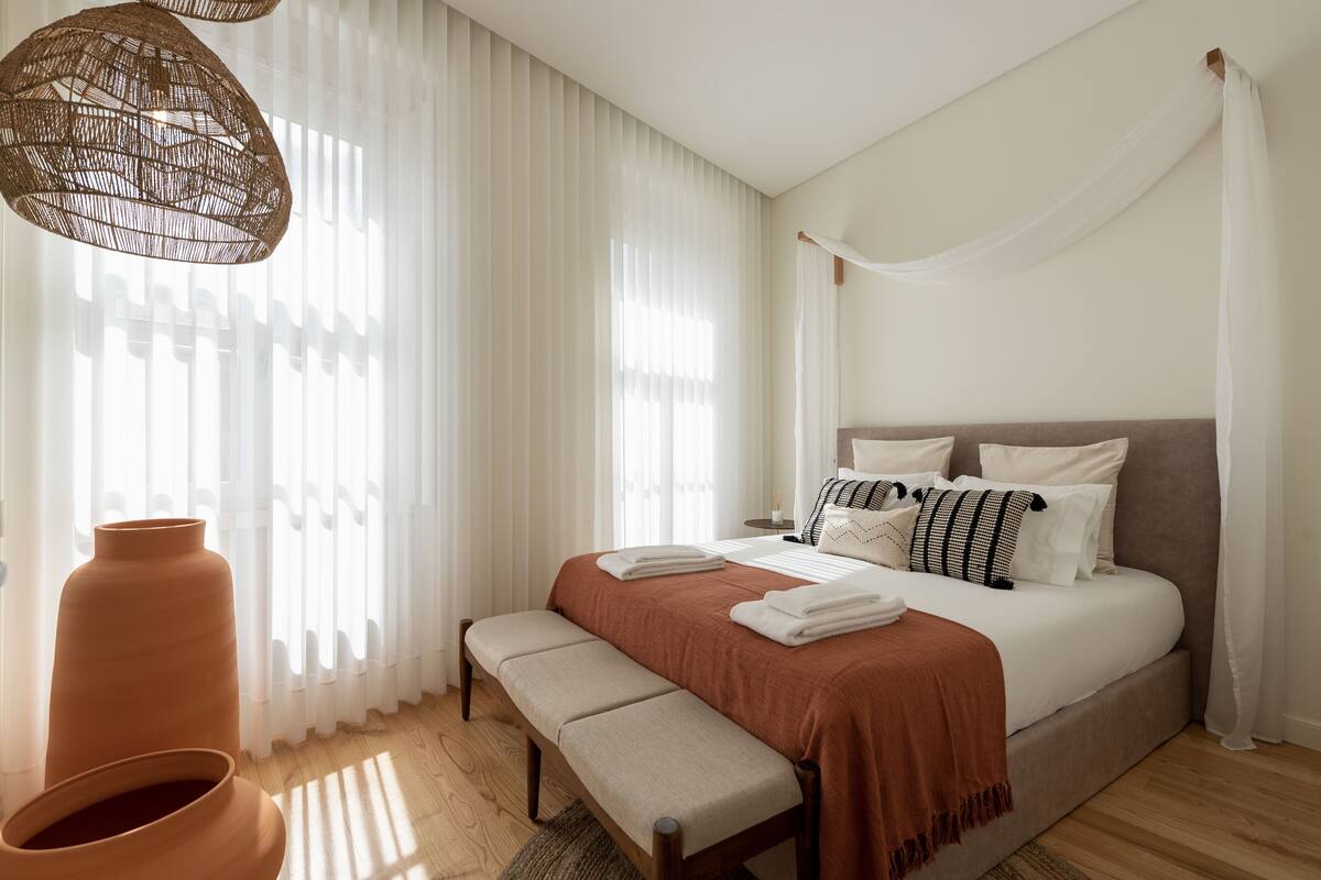 A bedroom with a large bed, a bench, and a large vase.
