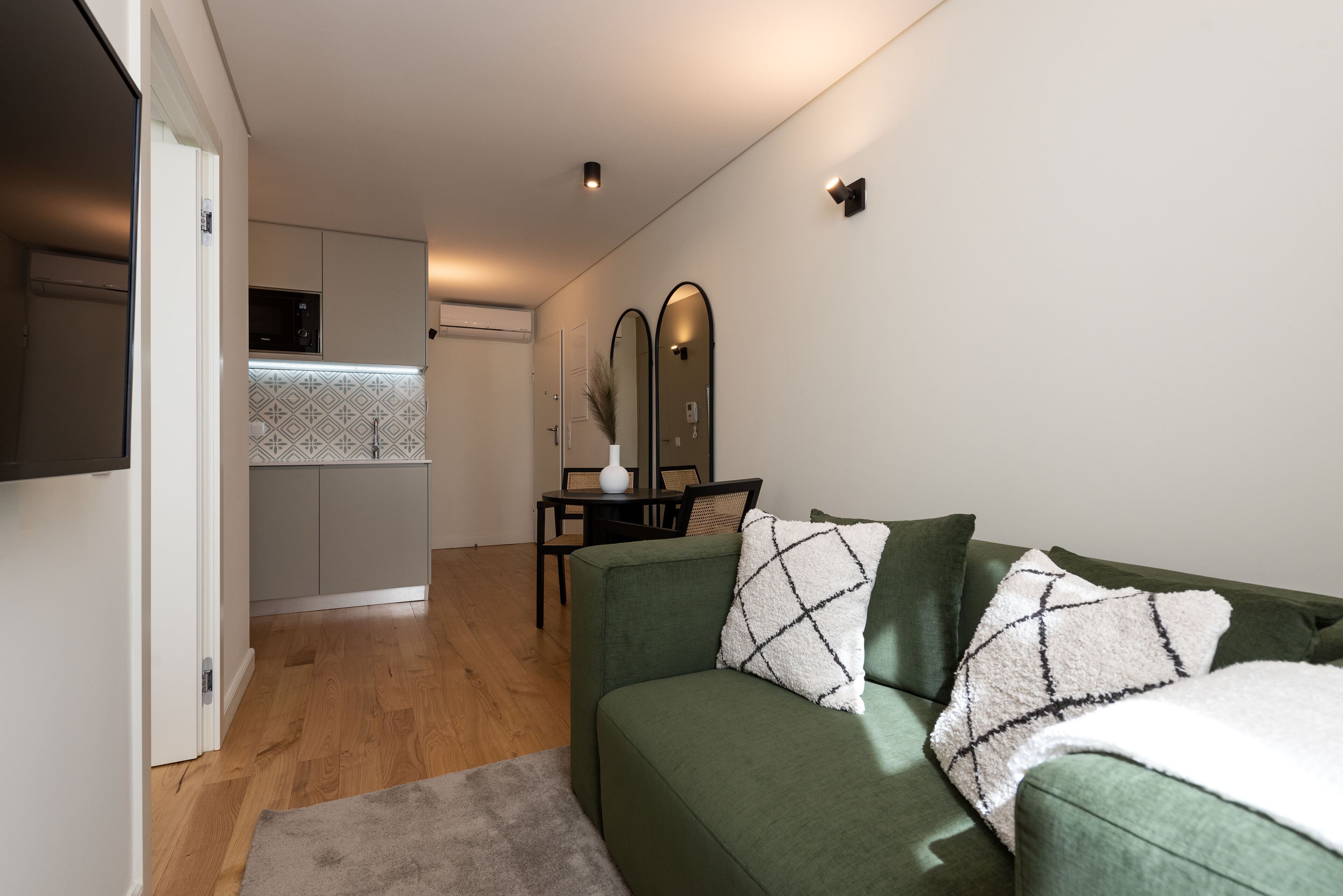 Un salon moderne avec un canapé vert, une petite table et une cuisine en arrière-plan.