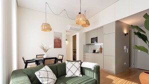 Una sala de estar moderna con un sofá verde, dos lámparas colgantes, un comedor con mesa y sillas, y una cocina con armarios y electrodomésticos.