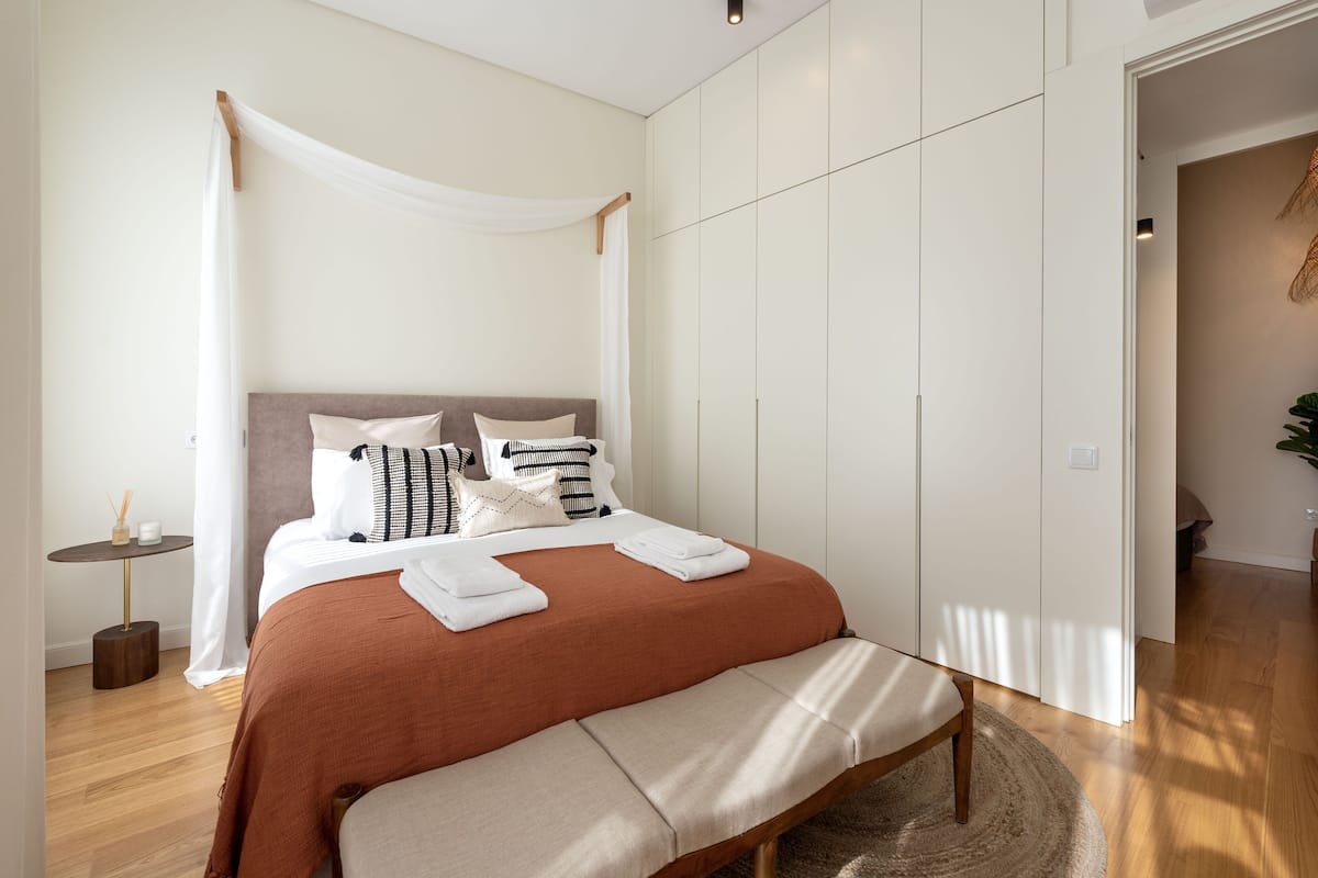 A modern bedroom with a large bed, a bedside table, a bench, and a wardrobe.