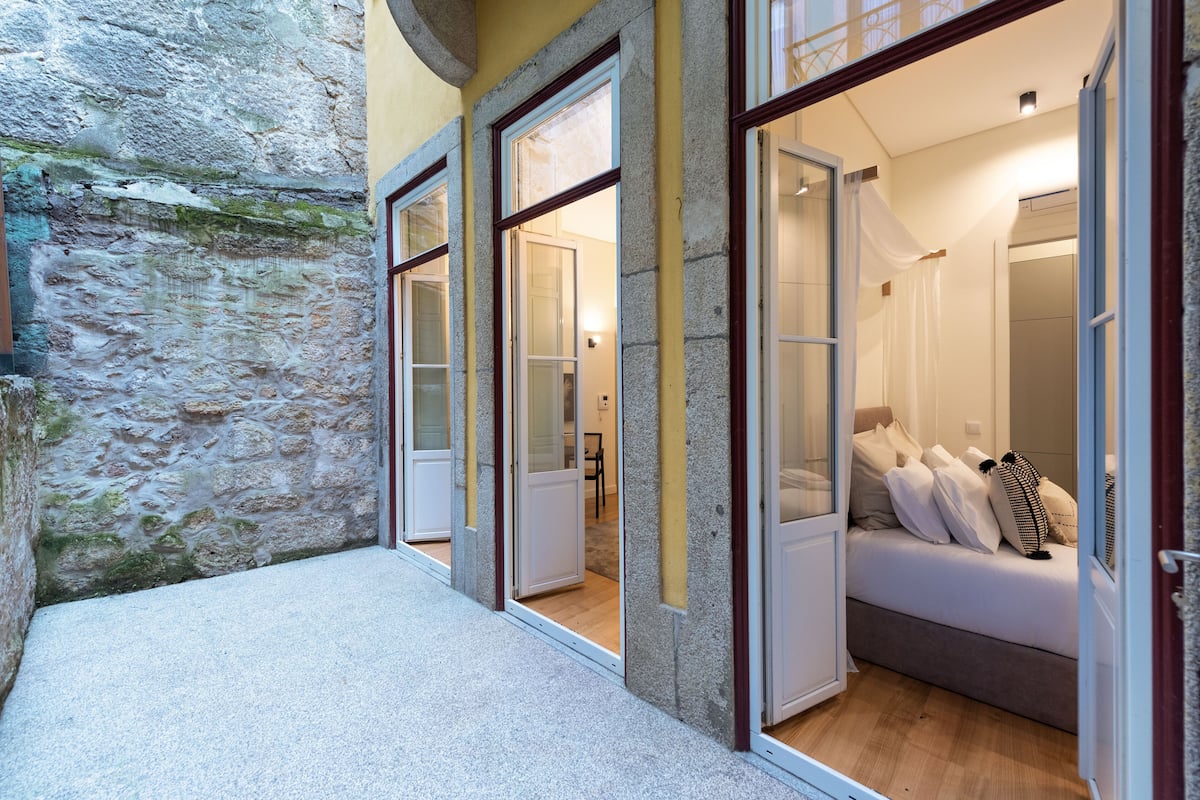 A narrow corridor with stone walls and a small room with a bed and a nightstand.