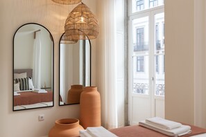 Ein Hotelzimmer mit Bett, zwei Spiegeln, einem Fenster mit Blick auf Gebäude und zwei großen Vasen auf dem Nachttisch.