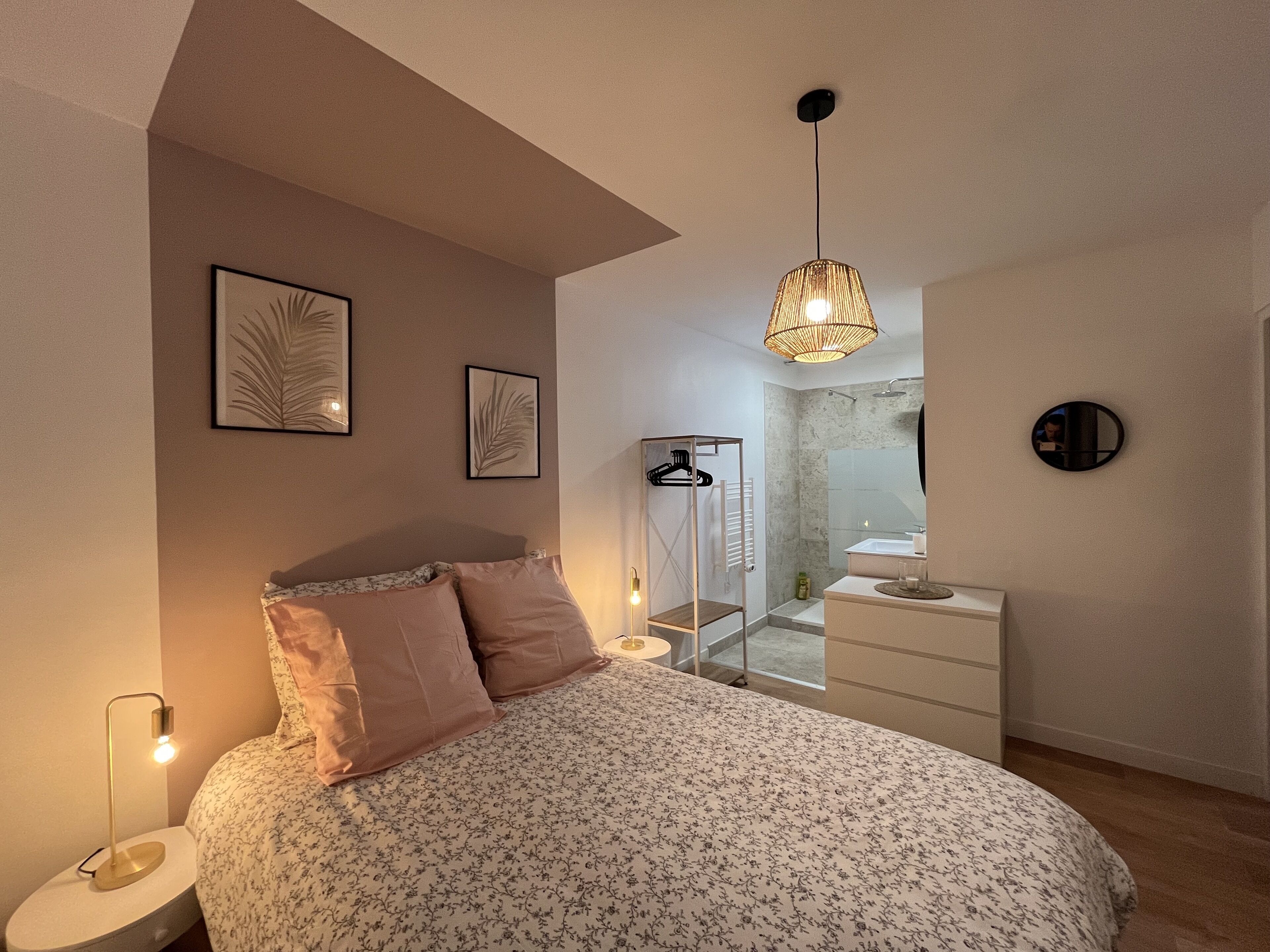 Un dormitorio moderno con cama, lámpara de noche y baño visible a través de un separador de vidrio.