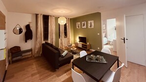A living room with a sofa, a dining table with chairs, a TV, and a ceiling light. - 🌟 Cosy Gannat 🌟 (Gannat)