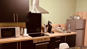 A modern kitchen with dark cabinetry, a stainless steel range hood, a microwave, a stove, and a refrigerator. There is a wooden countertop, a sink, and a dining area with a table and chairs. - 🌟 Cosy Gannat 🌟 (Gannat)