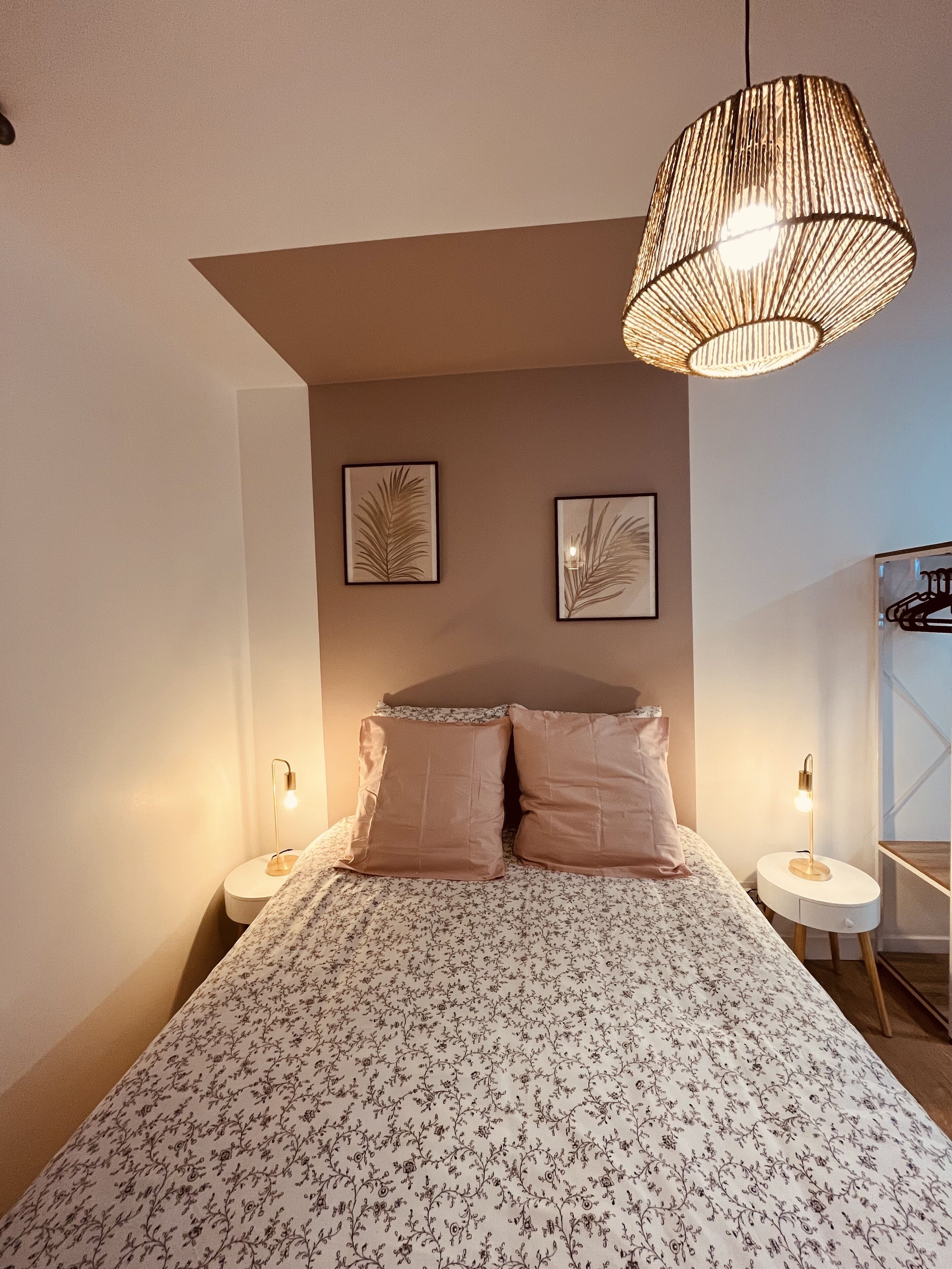 A bedroom with a large bed, two wall-mounted lamps, and two framed leaf designs on the wall.