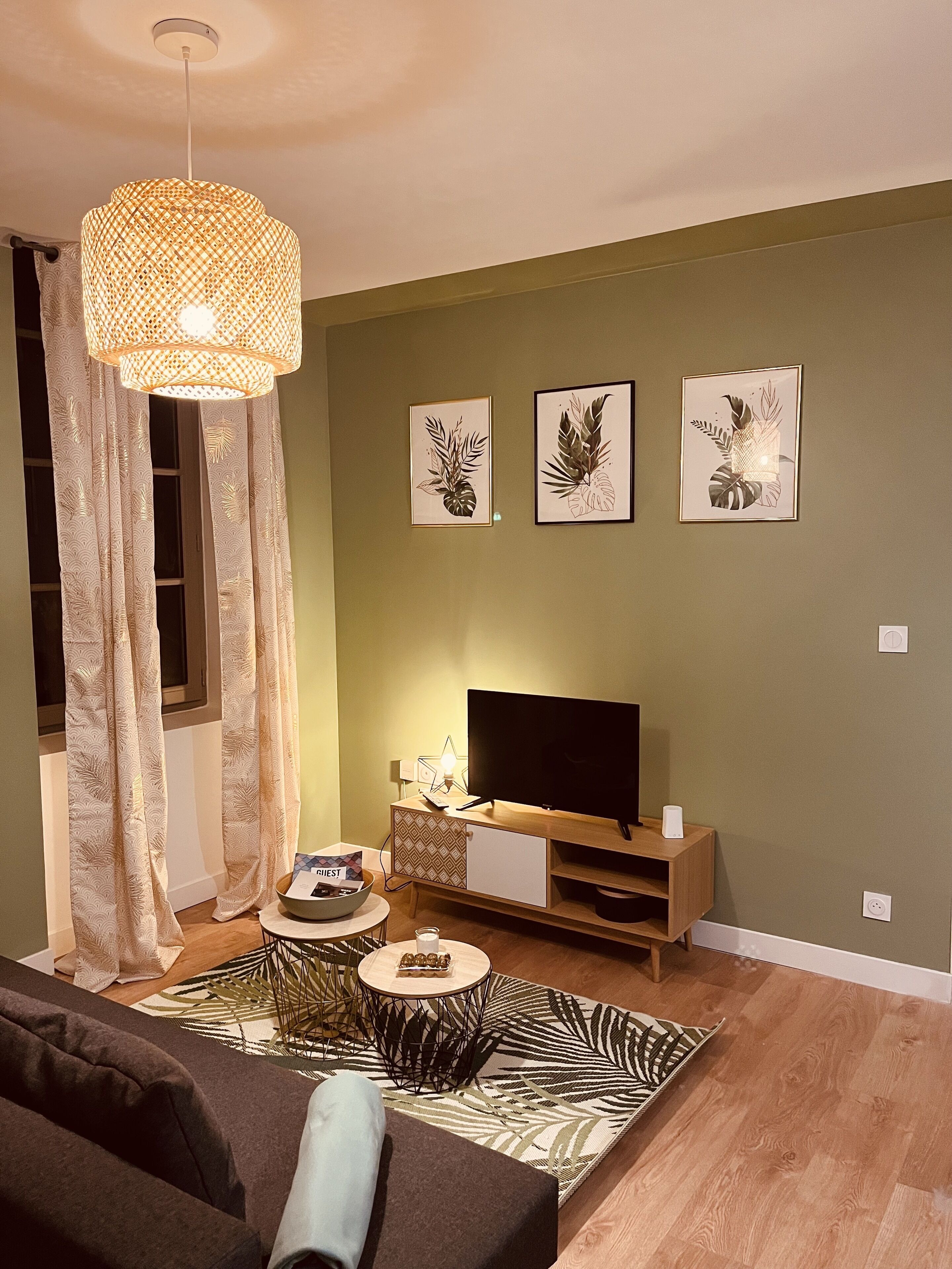 Una sala de estar con televisor, un tapete estampado, un sofá, una mesa de centro y un accesorio de iluminación decorativo.