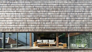 Una casa moderna con fachada de madera y balcón de vidrio que tiene un sofá y una mesa de centro.
