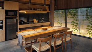 Una cocina moderna con una mesa y sillas de madera, horno integrado y un ventanal con vistas a la vegetación.