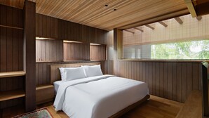 Un dormitorio con cabecera de madera, cama con ropa de cama blanca, estante de madera y ventana con persianas.