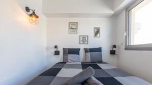 Ein ordentlich bezogenes Bett mit karierter Bettdecke, zwei Wandlampen und motivierende Plakate an der Wand.