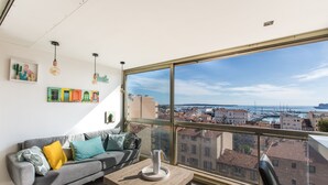A modern living room with a large window, a grey sofa, and a wooden coffee table. - Admire Panoramic Ocean Views Thru Walls of Windows (Cannes)