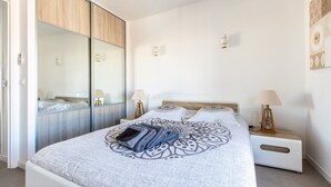 A modern bedroom with a large bed, a wardrobe with a mirror, bedside lamps, and a wall-mounted light fixture. - Admire Panoramic Ocean Views Thru Walls of Windows (Cannes)
