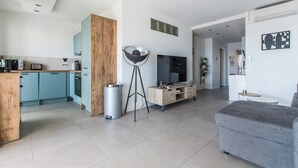 A modern kitchen with light blue cabinets, a wooden accent wall, a large black floor lamp, and a grey sofa in a living area. - Admire Panoramic Ocean Views Thru Walls of Windows (Cannes)