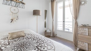 Ein Schlafzimmer mit einem großen Bett, einem Nachttisch, einer Lampe, einem Schminktisch und einem Fenster mit Vorhängen.