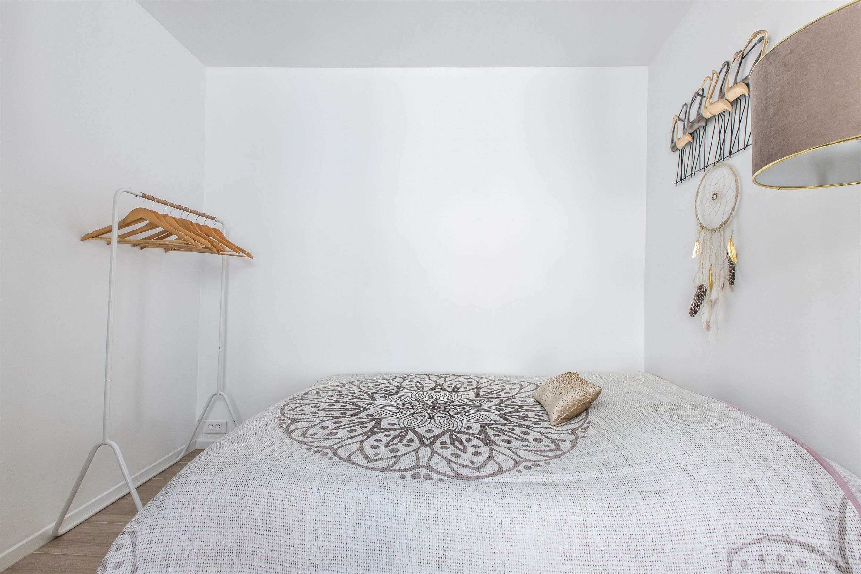 Une chambre à coucher au style minimaliste, avec une couvre-lit à motifs, un porte-manteau en bois et un attrape-rêves.