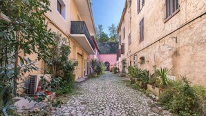 Une ruelle pavée bordée de bâtiments des deux côtés, dont certains sont dotés de balcons et de plantes.