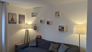 Ett modernt vardagsrum med en grå soffa, två golvlampor och flera vägghängda hyllor med böcker och dekorativa föremål.