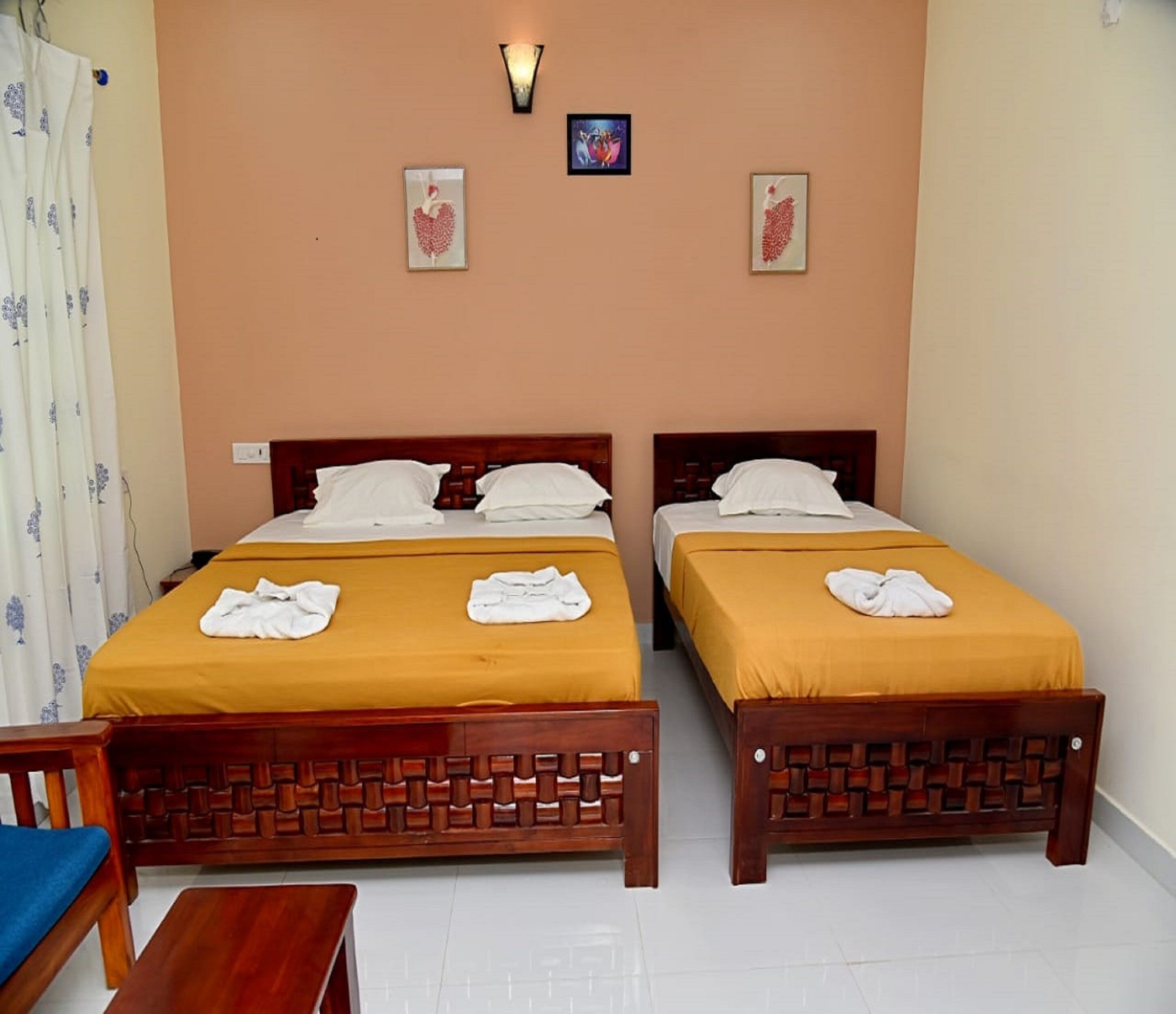 A hotel room with two beds, each with a wooden headboard and yellow bedding. There are two wall-mounted light fixtures and two framed pictures on the wall.