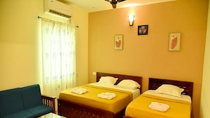 A hotel room with two single beds, a sofa, a small table, and a ceiling fan. - Nilton Bay Residency (Tindivanam)