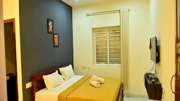 A bedroom with a bed, a ceiling fan, a window with blinds, and a TV mounted on the wall.