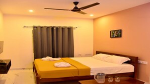 A hotel room with a bed, a bedside table, a ceiling fan, and a window with curtains. - Nilton Bay Residency (Tindivanam)