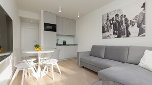 A modern living room with a grey sofa, a dining table with chairs, and a kitchen area with white cabinets and a black microwave. - Spacious Apartment | Center | Workspace | Balcony (Warszawa)