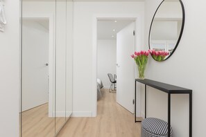 A hallway with a bed, a chair, a console table with a mirror, and a vase of flowers.