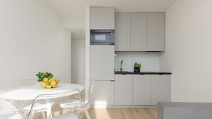 A compact kitchen with white cabinets, a microwave, and a small countertop. There is a dining table with chairs and a bowl of fruit. - Spacious Apartment | Center | Workspace | Balcony (Warszawa)