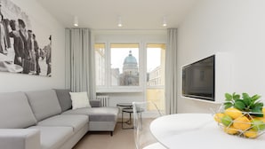 A modern living room with a grey sofa, a dining table with a white tablecloth, and a view of a building with a dome through large windows. - Spacious Apartment | Center | Workspace | Balcony (Warszawa)