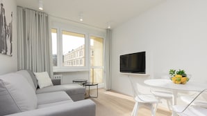 A modern living room with a grey sofa, a flat-screen TV, a dining table with chairs, and a window with curtains. - Spacious Apartment | Center | Workspace | Balcony (Warszawa)