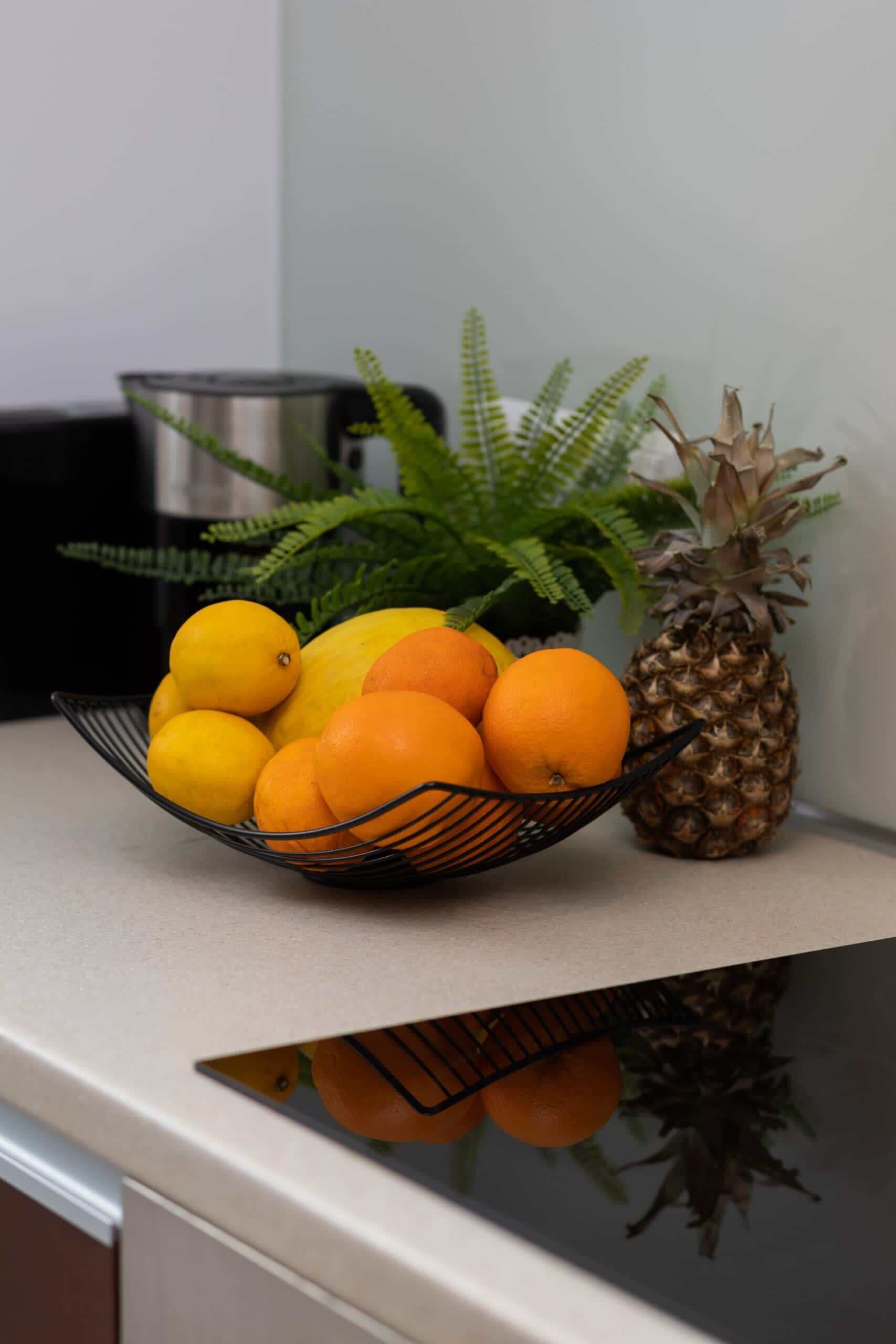 Un piano di lavoro in cucina con una ciotola di frutta contenente arance e un ananas.