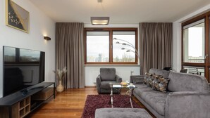 Ein modernes Wohnzimmer mit Flachbildfernseher, grauem Sofa und einem großen Fenster mit Vorhängen.