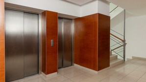 Ein moderner Aufzug mit Metalltüren und Holzvertäfelung, neben einer Treppe mit Glasgeländern.