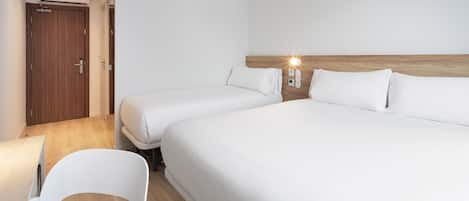 A hotel room with two beds, a wooden headboard, a white chair, and a desk.