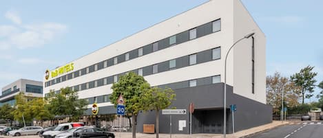 A modern hotel with a flat facade, multiple windows, and a parking lot with several cars.