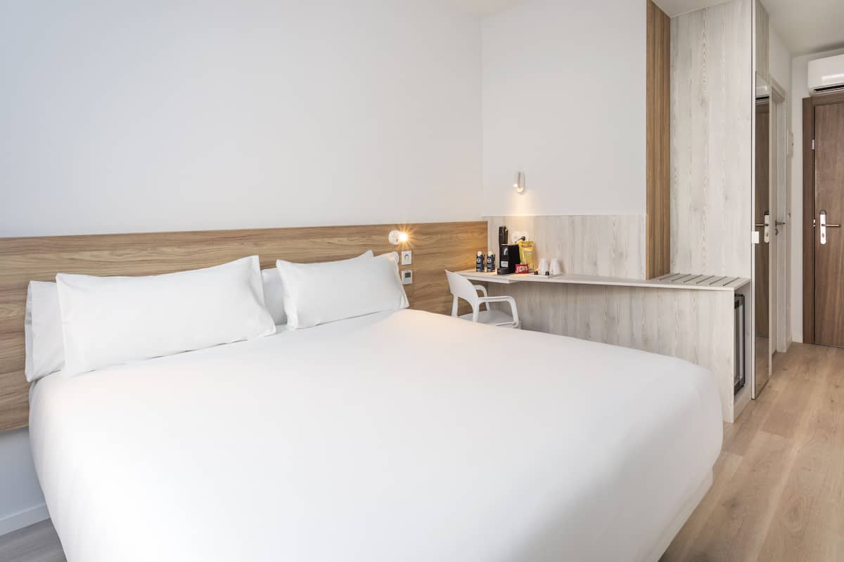 Une chambre d’hôtel avec un grand lit, un petit bureau avec une chaise, une table de chevet et une tête de lit en bois.