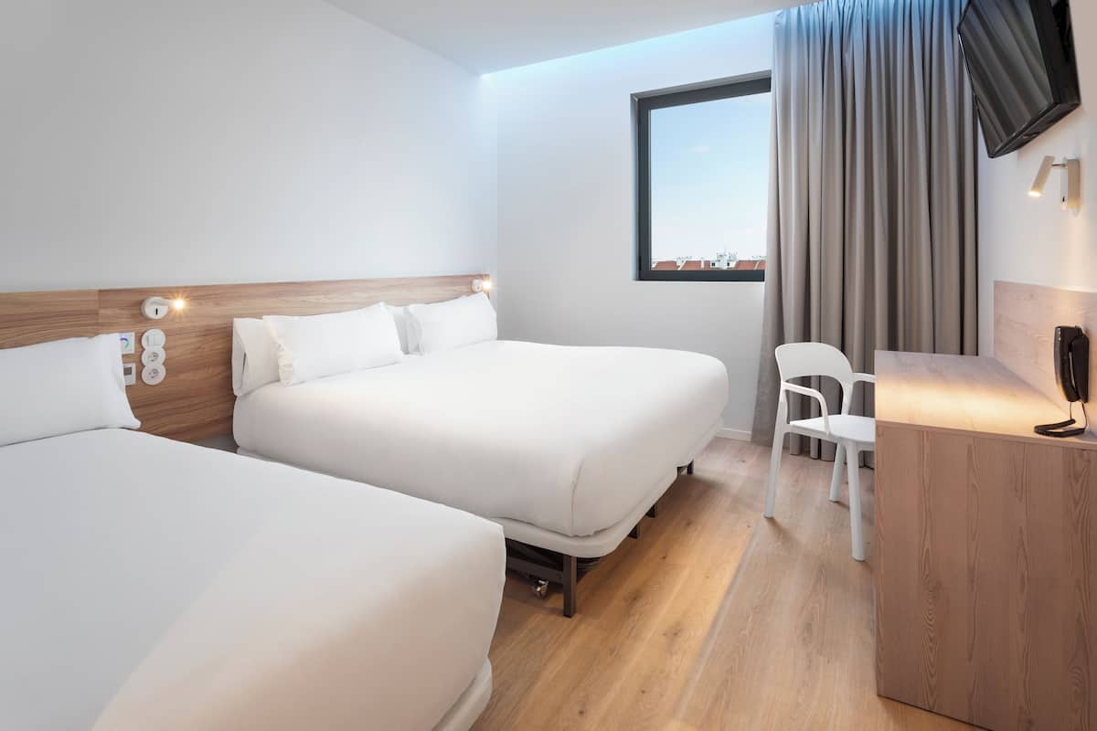 Une chambre d’hôtel avec deux lits, un bureau, une chaise et un téléviseur fixé au mur.