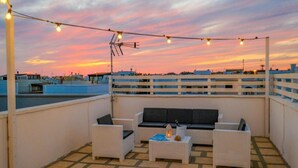A rooftop terrace with outdoor furniture, string lights, and a view of the city skyline at sunset. - CASAMARiNATSG- Sea View (Torre San Giovanni)