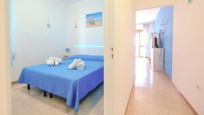 A bedroom with a blue bedspread, a bedside table with a lamp, and a painting on the wall. - CASAMARiNATSG- Sea View (Torre San Giovanni)