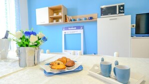 A room with a blue wall, a white cabinet, a microwave, and a table with a plate of muffins and blue cups. - CASAMARiNATSG- Sea View (Torre San Giovanni)