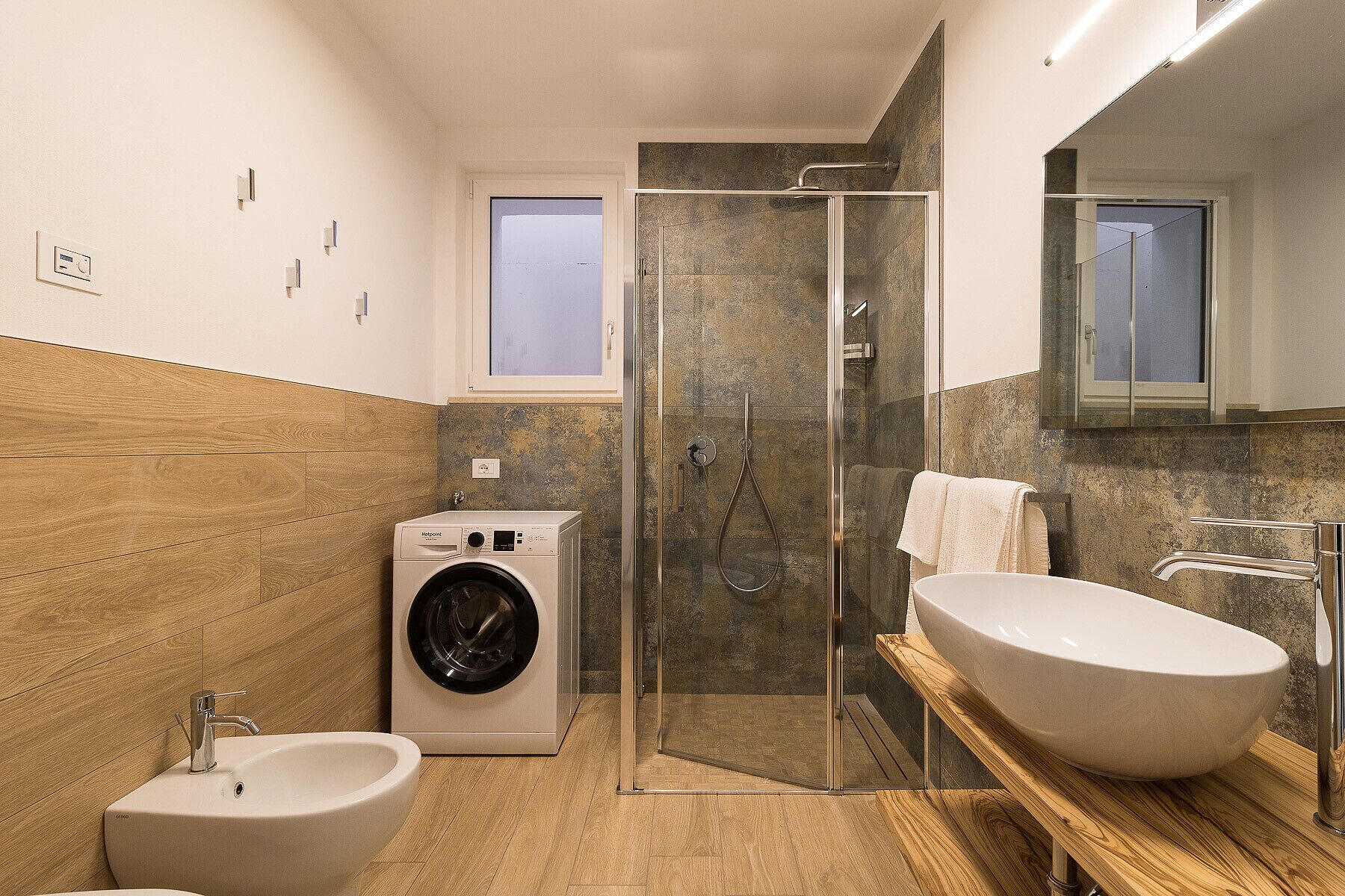 A modern bathroom with a glass-enclosed shower, a standalone sink, a toilet, and a washing machine.