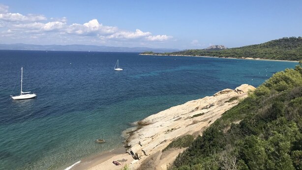 A coastal landscape with clear blue waters, a sandy beach, and rocky terrain.