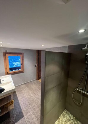 Een moderne badkamer met een douche, wastafel en een raam met uitzicht op een besneeerd landschap.