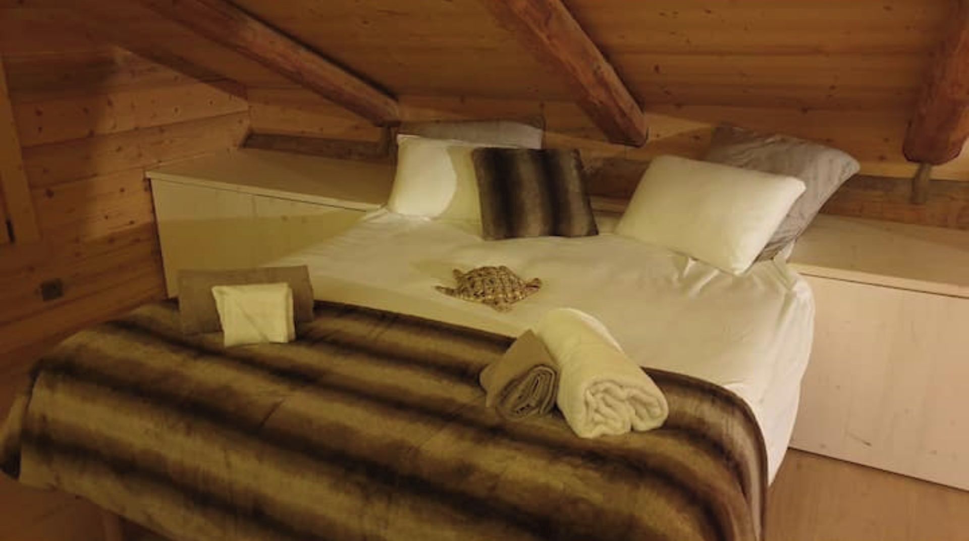 Un dormitorio de cabaña de madera con una cama, almohadas, una colcha y una tortuga sobre la cama.