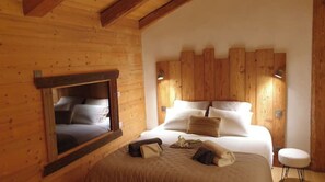Een slaapkamer in een houten hut met een bed, kussens en een klein krukje.