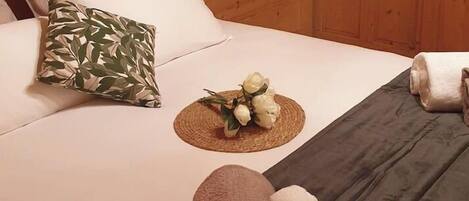 Habitación de cabaña de madera con una cama, almohadas, una toalla enrollada y una mesita con un arreglo floral.