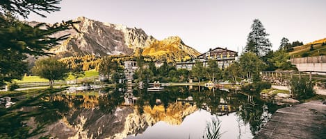 A mountain lodge with a reflection in a lake, surrounded by trees and a wooden deck.