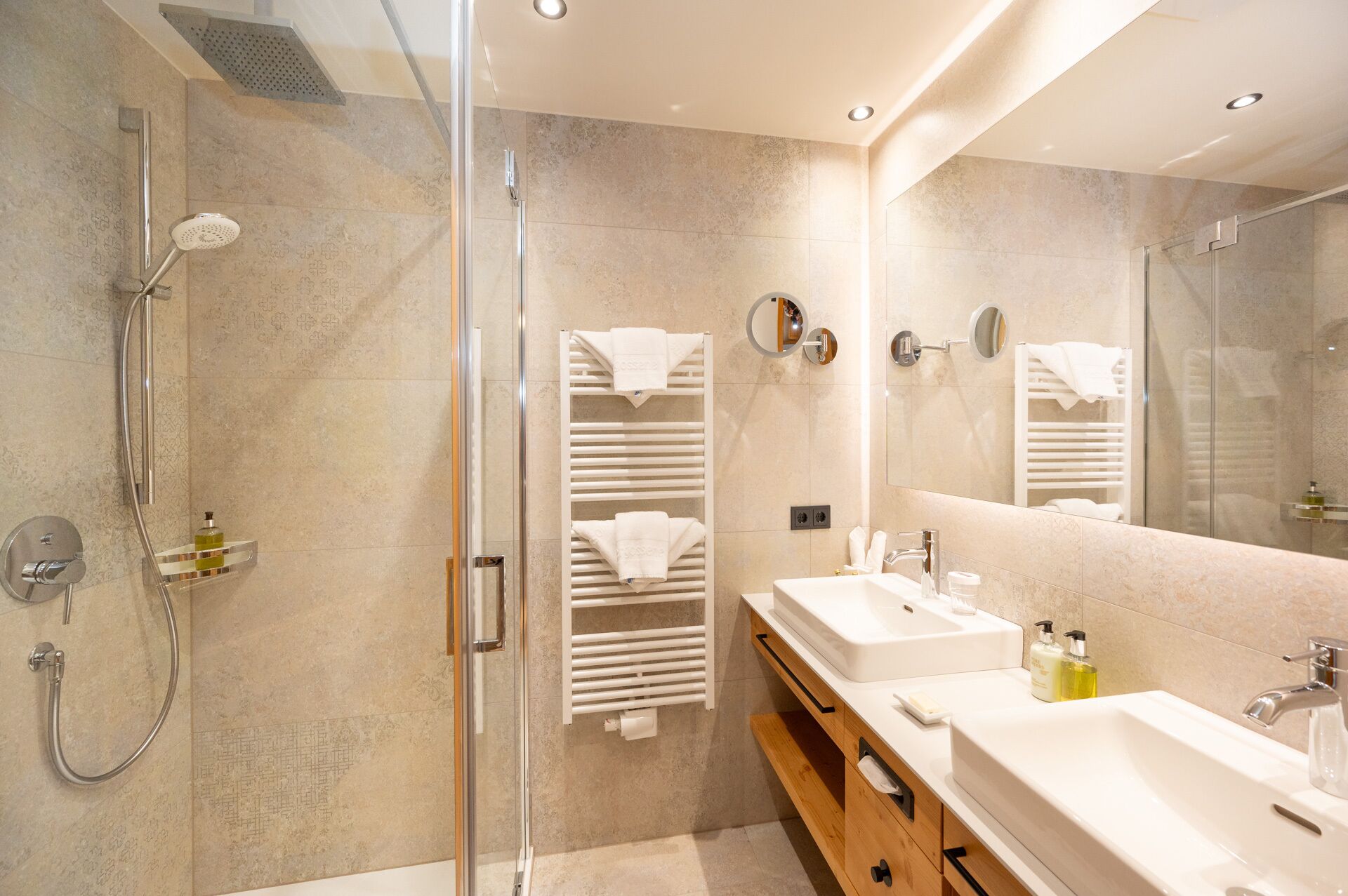 Un baño moderno con ducha de vidrio, dos lavamanos y un espejo grande.