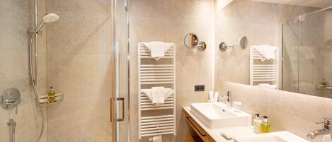 Un baño moderno con ducha de vidrio, dos lavamanos y un espejo grande.
